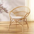 Wicker chair with a white cushion on a wooden floor, with a plant in the background.