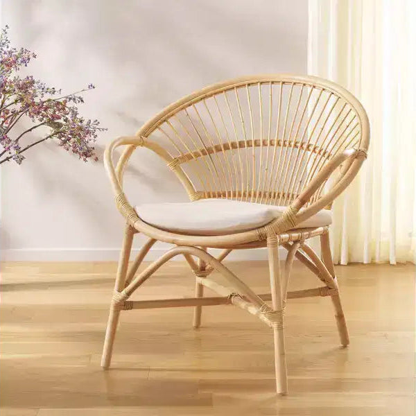 Wicker chair with a white cushion on a wooden floor, with a plant in the background.
